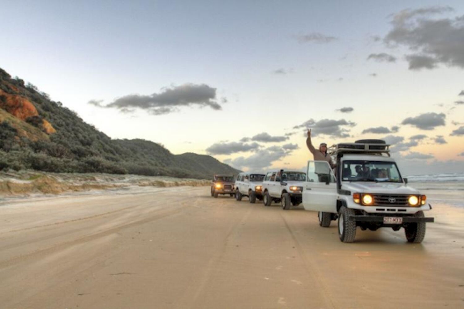 4WD convoy driving along 75 Mile Beach at sunset on a K'gari (Fraser Island) tag-along tour
