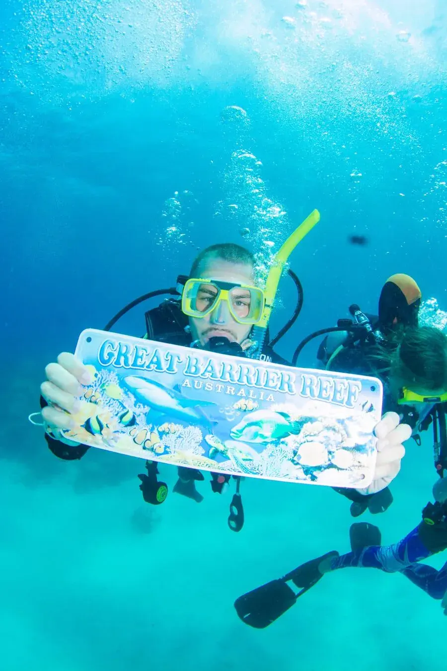 Traveller scuba diving on the Great Barrier Reef holding a Great Barrier Reef sign